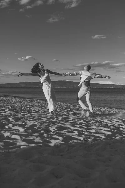 男と女が踊り、バカンス幸せなカップル。ビーチ、海岸を走る愛のカップル。愛のカップルは、楽しみ、海とのスカイラインの背景を持つ手を保持しています。概念をちょうど結婚結婚式、. — ストック写真