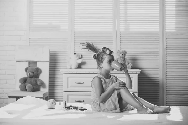 Niña con la cara tranquila bebe té y juega con cosméticos — Foto de Stock