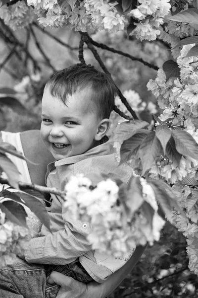 可爱快乐的男孩在母亲怀抱中盛开的花朵中微笑 — 图库照片