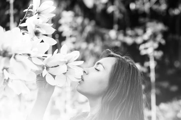 girl smelling pink, blossoming, magnolia flowers from tree