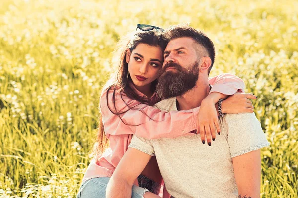 Homem com barba e mulher senta-se no dia de primavera grama. Casal apaixonado passar o tempo ao ar livre e abraços. Casal em rostos sonhadores sentados no prado, natureza no fundo. Conceito de lazer primavera — Fotografia de Stock