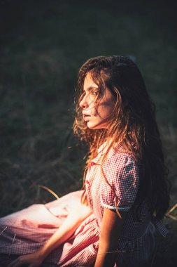 Güneşli çayır üzerinde vintage elbiseli güzel romantik kız. Yan görünümü rüya gibi olan kadın kıvırcık saçlar çimde oturma. Masal ve fantezi kavramları
