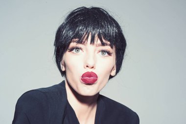 Yüz öpüşmeyle kız siyah resmi ceket giyer. Siyah peruk Bayan gri arka plan üzerinde olun. Kadın çekici kırmızı dudaklar ile kameraya benziyor. Öpücük ve ruj kavramı.