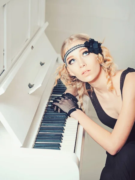 Молодая актриса с голубыми глазами смотрит вверх, лежа на открытой клавиатуре белого фортепиано — стоковое фото