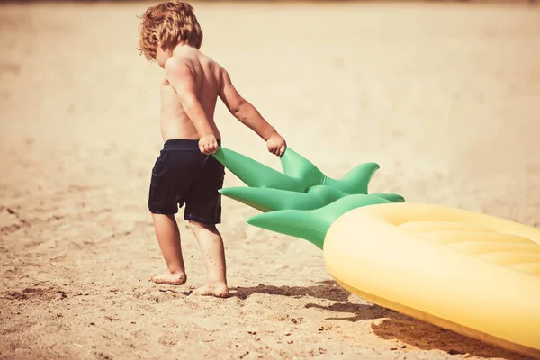 Piccolo bambino tirare materasso ad aria sulla sabbia. Vacanze estive e viaggi verso l'oceano. Materasso gonfiabile all'ananas, attività e gioia. Maldive o Miami Beach. bambino sul mare dei Caraibi alle Bahamas . — Foto Stock