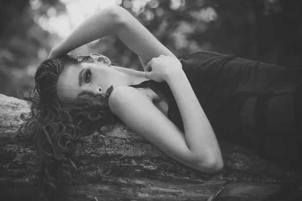 Mujer con peinado rizado en verano. Mujer con el pelo largo morena relajarse en el árbol en la naturaleza. Cuidado del cabello, terapia y tratamiento. Chica con cara de maquillaje, belleza. Modelo de moda con look glamour — Foto de Stock