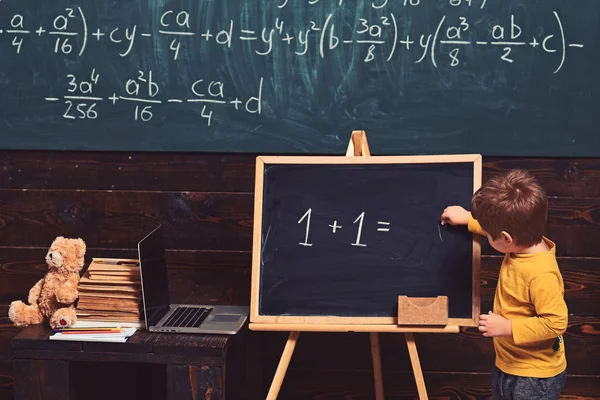 Education concept. Little boy solving equation on chalkboard. Preschool training for smart kid