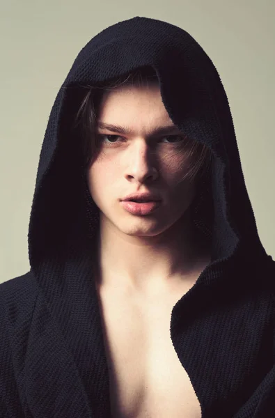 Guy on confident face in black hood, grey background. Man with smooth skin on face, neck and chest looking at camera. Masculinity concept. Macho in black bathrobe with hood, close up — Stock Photo, Image