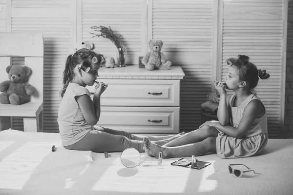 Děti sedí na posteli s rtěnky, laky na nehty a zrcadlo — Stock fotografie