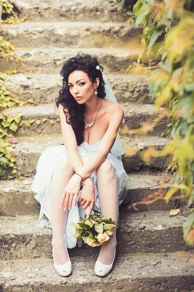 Gelin moda beyaz elbiseli. Gelin düğün buket ile oturup merdiven üzerinde — Stok fotoğraf