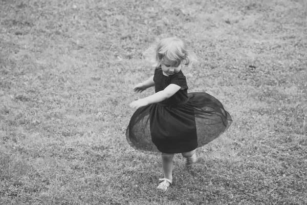 Menina com cabelo loiro girar em vestido preto na grama — Fotografia de Stock