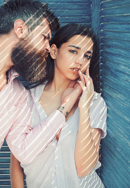 Heat concept. Couple chilling near jalousie, stripes of sunlight and shadow on faces. Couple in love on calm faces near turquoise jalousie. Girl in unbuttoned shirt and man with beard.