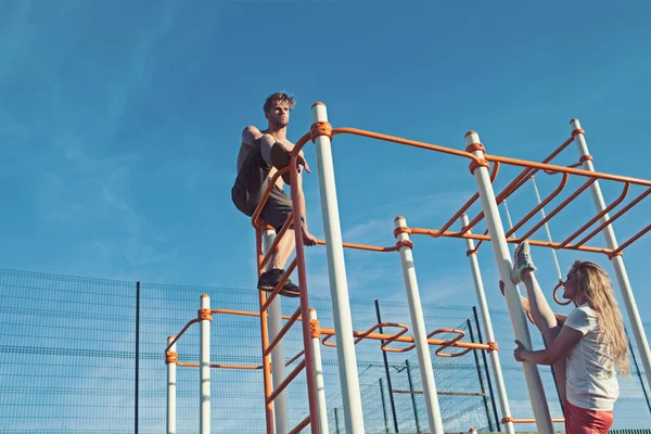 Adam atlet üst ve kadın split bacak üzerinde tırmanmaya. Çift eğitim metal orman spor salonunda spor. Sporcu ve sporcumuz maymun barlarda. Spor pilates ve egzersiz kavramı