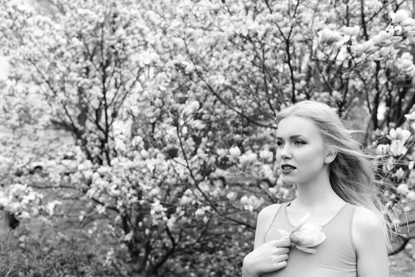 pretty girl hold magnolia flower at blossoming tree, spring garden
