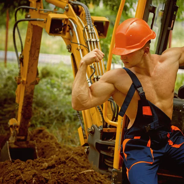 Conceito de engenheiro. Forte engenheiro na cabine da escavadora. Engenheiro flex bíceps e músculo tríceps. Engenheiro em uniforme de trabalho no local da escavação. Sinta o poder — Fotografia de Stock