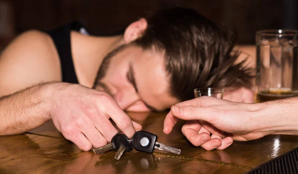 Предупреждение о ДТП. Алкоголик с ключами от машины спит на барной стойке. Человек после употребления крепкого алкоголя и пива в пабе. Алкоголичка с алкогольным напитком. Алкогольная зависимость и вредная привычка — стоковое фото