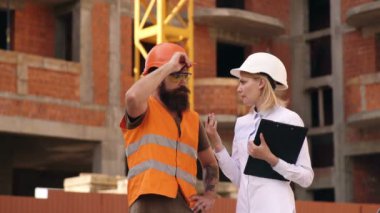 Şantiyede 4k Mühendisler planları bakarak ve proje tartışıyor. İki genç mühendis adam ve kadın şantiyede bir tartışma var. İnşaatüzerine inşaatçılar.