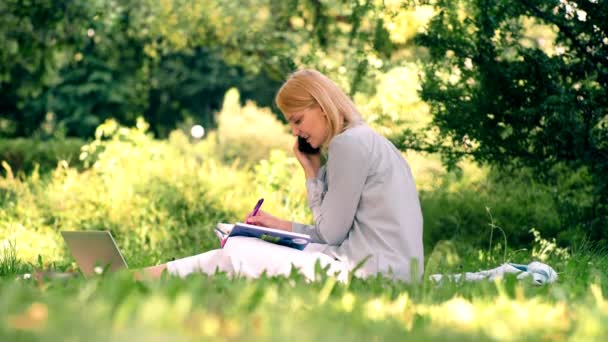 Giovane studentessa che studia seduta nel parco. Bellissimo giardino. Attività per il tempo libero in primavera ed estate . — Video Stock