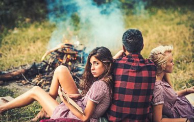 Şenlik ateşi kadınlara olan adam. Erkek ve kız kitap okumak. Arkadaşlar kamp tatil keyfini çıkarın. İnsanlar yaz doğa ateşe dinlenin. Aşk üçgeni, hile ve ilişkiler