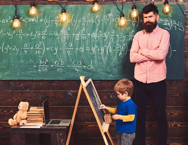 厳密な数学の先生が生徒の作業をチェックします。金髪の少年が黒板に方程式を解きます。幼児教育の概念 — ストック写真