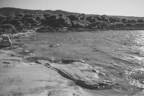 Spiaggia rocciosa bagnata da onde, mare e verde foresta tropicale sullo sfondo. Spiaggia rocciosa di mare, acqua limpida, trasparente vicino a grande pietra, roccia. Paesaggio naturale nella soleggiata giornata estiva. Concetto natura . — Foto Stock