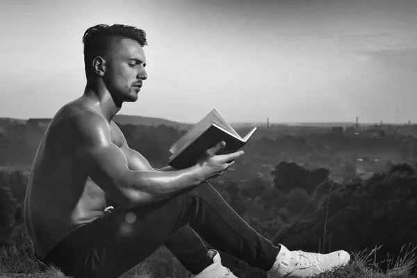Pensivo homem muscular com livro ao ar livre — Fotografia de Stock