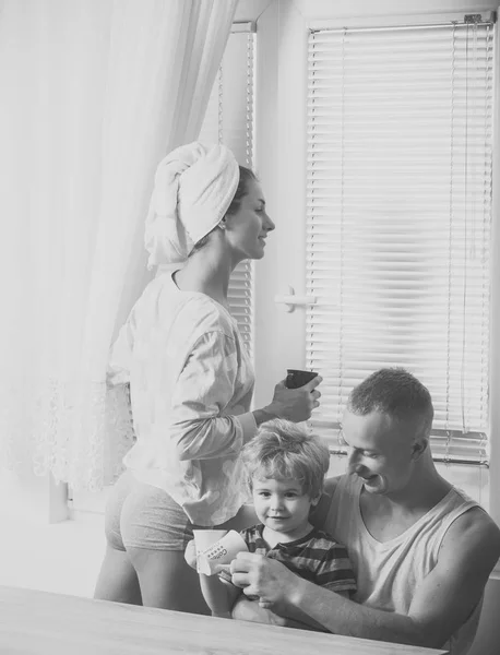 Ranní rutinní pojetí. Matka a otec a dítě sedí u stolu v ráno. Rodina s úsměvem pití čaj, káva. Šťastná rodina trávit čas společně, bílý interiér a okno na pozadí. — Stock fotografie