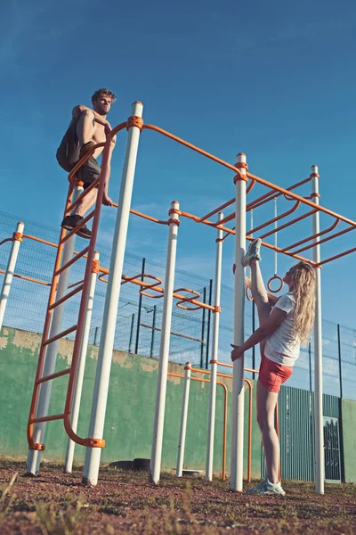 Sportman en Sportvrouw van monkey bars. Sport paar opleiding in metalen jungle gym. Man atleet klimmen op boven- en vrouw split been. Sport training en pilates concept — Stockfoto