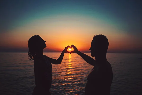 Couple on the sunset beach at tropical resort make heart from hands Travel concept. — Stock Photo, Image