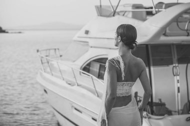 Genç güzel esmer kadın rahatlatıcı rıhtım tekne, yaz günü sunset yakınında. Kadın moda giysiler içinde lüks yat, dikiz durumda. Lüks hayat kavramı.