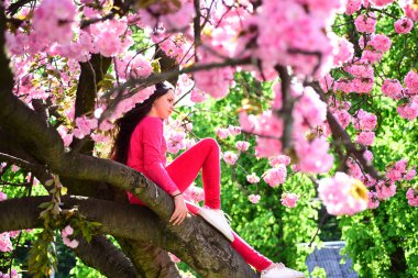 Keeping the chic look by wearing a pair of sneakers. Pretty girl with fashion look. Fashion clothing for spring. Fashionable young lady on flowering tree. Little girl in fashion wear in spring garden