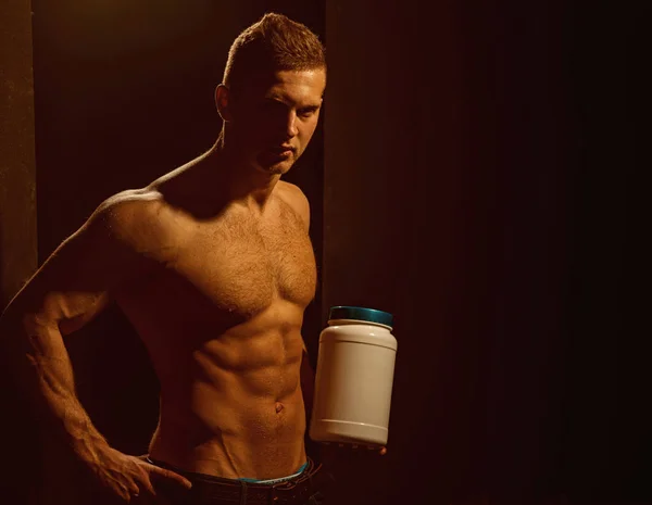 Affecting muscle growth. Man use sport vitamin supplements for muscle building. Sport nutrition and vitamin diet. Athletic man hold vitamin bottle in strong arms. Healthy diet and fitness, copy space