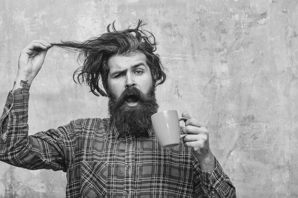 Удивленный бородатый мужчина тянет стильные волосы с голубой чашкой — стоковое фото