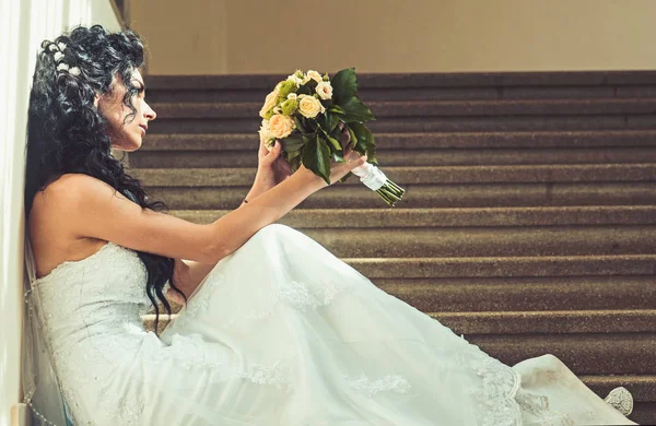 Mode vrouw met bruiloft boeket zitten op de trap. Mode bruid met bruids make-up en kapsel in witte jurk met bloemen — Stockfoto