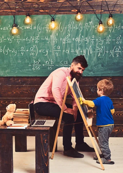 Tutor explicando matemáticas a un niño pequeño. Volvió chico limpiando pizarra con tela amarilla. Papá sentado en la mesa mientras habla con el hijo — Foto de Stock