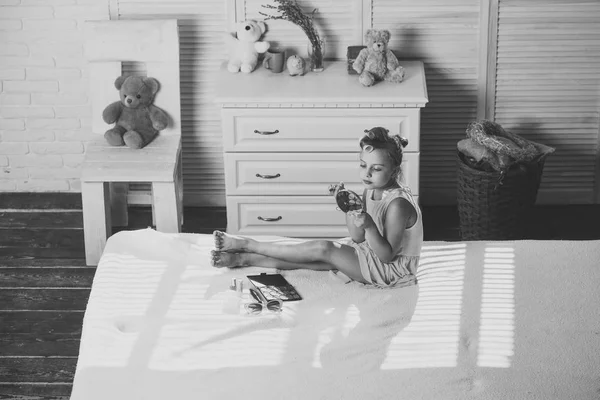 Criança senta-se na cama com batom brilhante e cosméticos — Fotografia de Stock