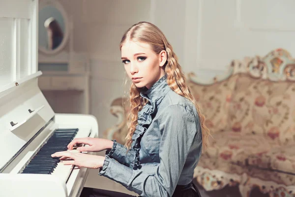 Junges viktorianisches Mädchen in einem zarten blauen Kleid, das Klavierspielen lernt. schöne blonde Frau mit lockigem Haar sitzt im Zimmer mit Vintage-Sofa. privates Bildungskonzept — Stockfoto