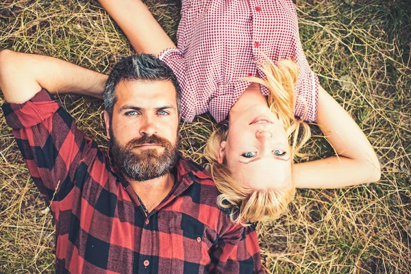 Couple in love lying on grass in forest or park. Romantic date in nature, love and relationship concept. Bearded man with blue eyes and beautiful blond girl in retro dress enjoying summer evening — Stock Photo, Image