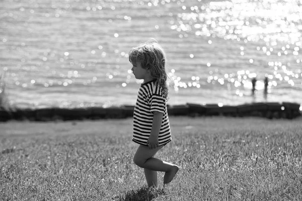 Bonito menino em tshirt listrada caminha na grama verde — Fotografia de Stock