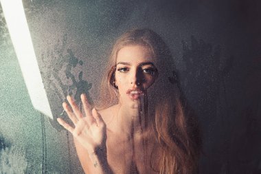 Kalp şeklinde pencere camına yağmur damlaları. Su ile plastik levha arkasındaki seksi kadın bırakır. Kız makyaj ile daha önce su ile pencere bırakır. Duş ve hijyen kaplıca tedavisi. Moda güzellik ve aşk.