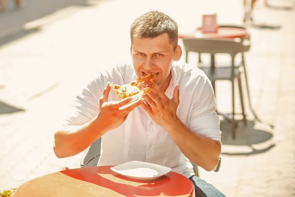 Człowiek zjeść kawałek pizzy w ulicznej kawiarni. Szczęśliwy macho cieszyć przekąska na słoneczny odkryty, dieta. Koncepcja żywność i dieta — Zdjęcie stockowe