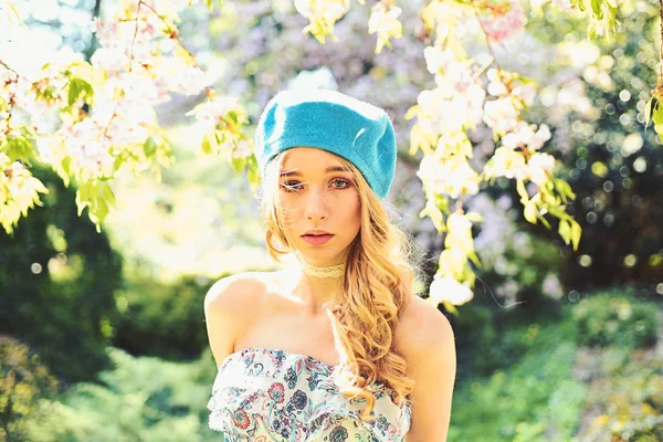 Mädchen mit ruhigem Gesicht, zarte Blondine in der Nähe von Sakura-Blumen, Naturhintergrund. Konzept im französischen Stil. junge Französin genießt die Natur. Dame trägt Kleid und blaue Baskenmütze spaziert an sonnigem Frühlingstag im Park. — Stockfoto