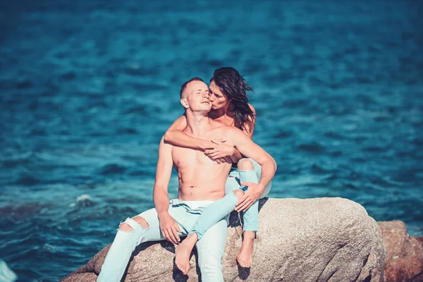 Casal apaixonado relaxar na pedra da praia. casal no amor topless bronzeado do sol em jeans na água do mar . — Fotografia de Stock