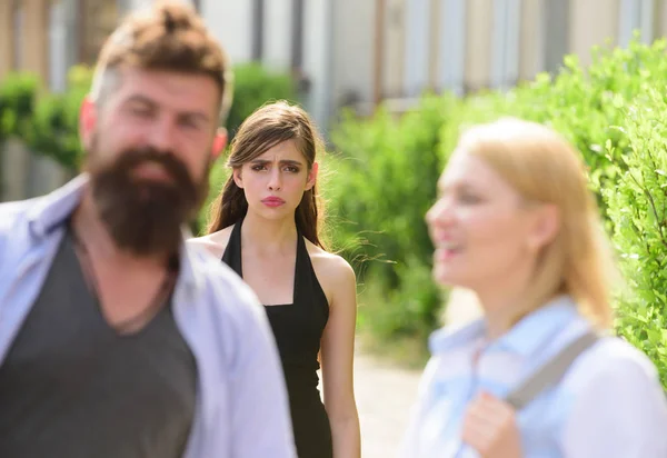 She seems jealous. Bearded man cheating his girlfriend with another woman. Unhappy girl feeling jealous. Jealous woman look at couple in love on street. Romantic couple of man and woman dating