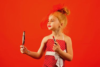 Moda ve güzellik, pinup stil, çocukluk. Küçük kız ruj ve ayna tutun. Şık elbise, makyaj kız çocuk. Kozmetik, güzellik ile Retro kız moda. Makyaj retro görünüm ve Kuaför.