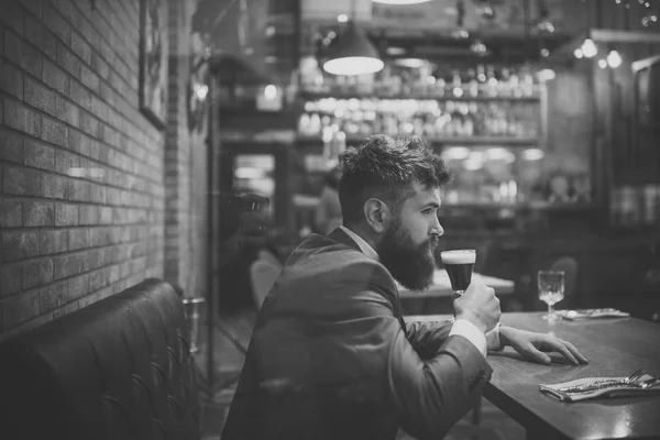 serious bar customer sit in cafe drinking ale. Beer time. Date meeting of hipster awaiting in pub. Businessman with long beard drink in cigar club. Bearded man rest in restaurant with beer glass.