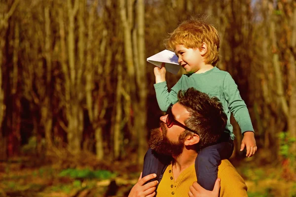 Flying is the perfect vocation for a man who wants to feel like a boy. Little son dream of flying on fathers shoulder. Child boy and father launch paper plane in park — Stock Photo, Image