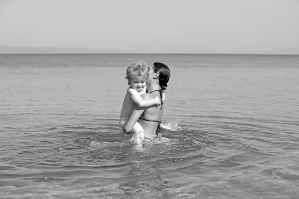 Madre con hijo pequeño e hija nadan en agua de mar en la playa . — Foto de Stock
