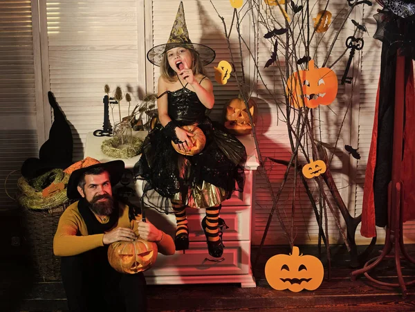 Wizard and little witch in hats carve pumpkins