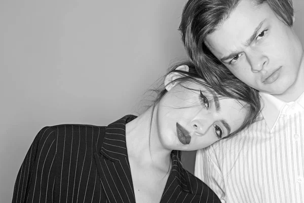 Pareja en caras tranquilas vestidas con ropa de moda. Chica con maquillaje se inclinan sobre el hombro masculino, fondo gris. Concepto de moda. Un par de modelos con estilo en la sesión de fotos de moda, espacio de copia . — Foto de Stock